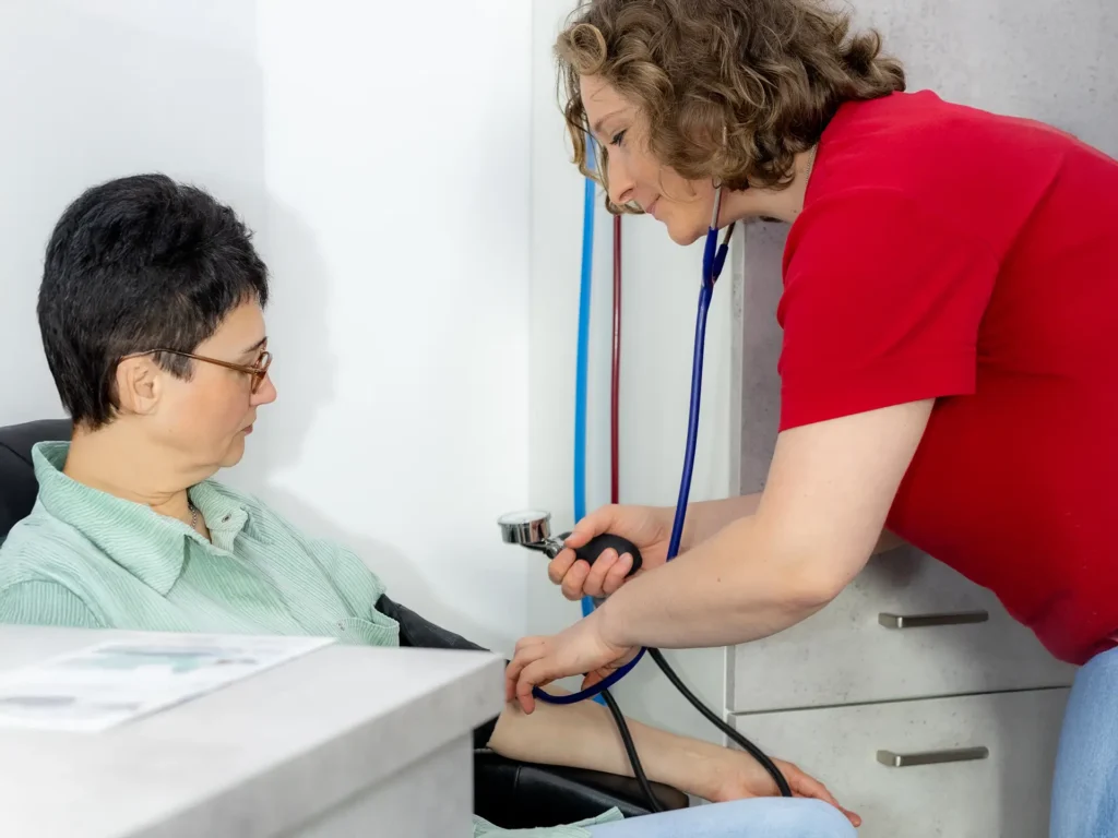 Eine medizinische Fachangestellte misst bei einer Patientin den Blutdruck mit einem manuellen Blutdruckmessgerät.